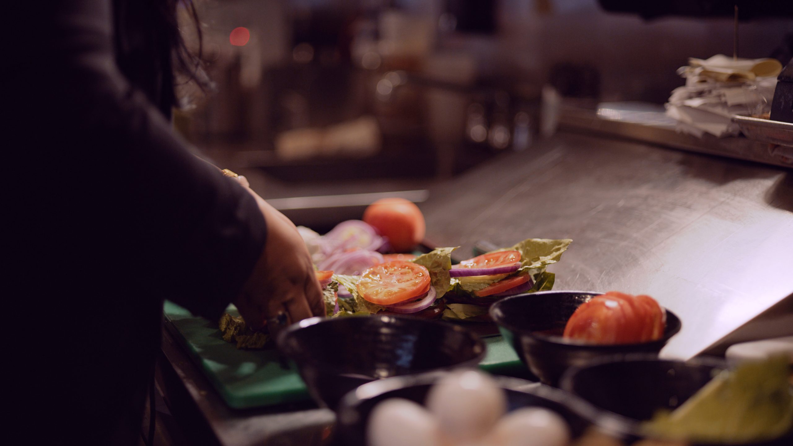 IU Jeepney NYC Filipino BBQ Pop Up Restaurant Closeup of lettuce, tomatoes and onions being assembled by a female chef with long black hair