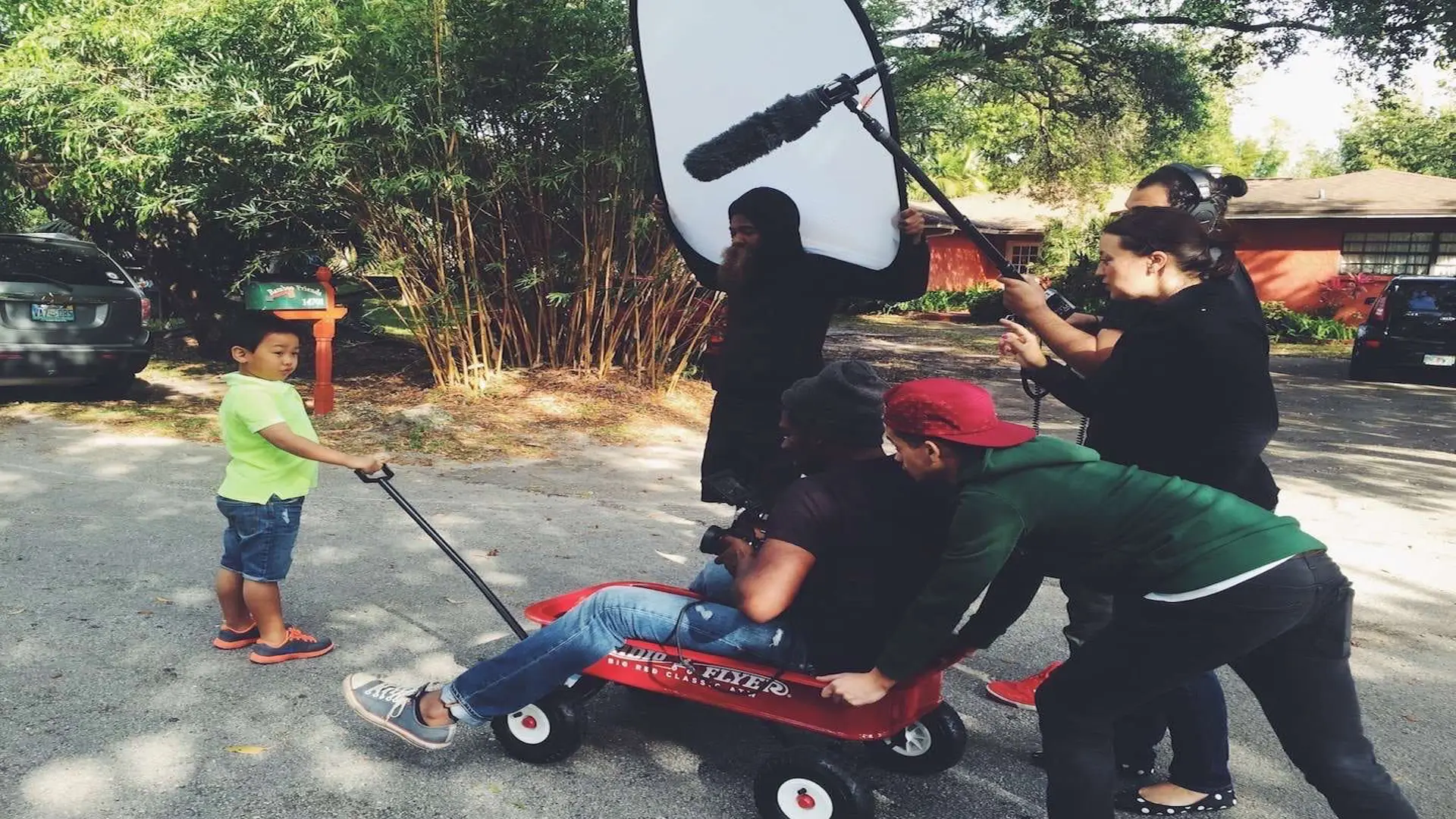 Purebred Breeders 20 Joshua sitting in a red metal wagon filming a boy holding the handle with crew around them.