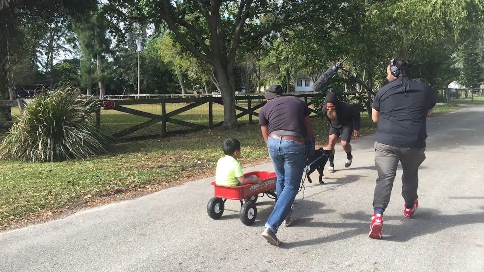 Purebred Breeders 18 View from behind of boy in a metal wagon cart being pulled along by a dog with crew around him