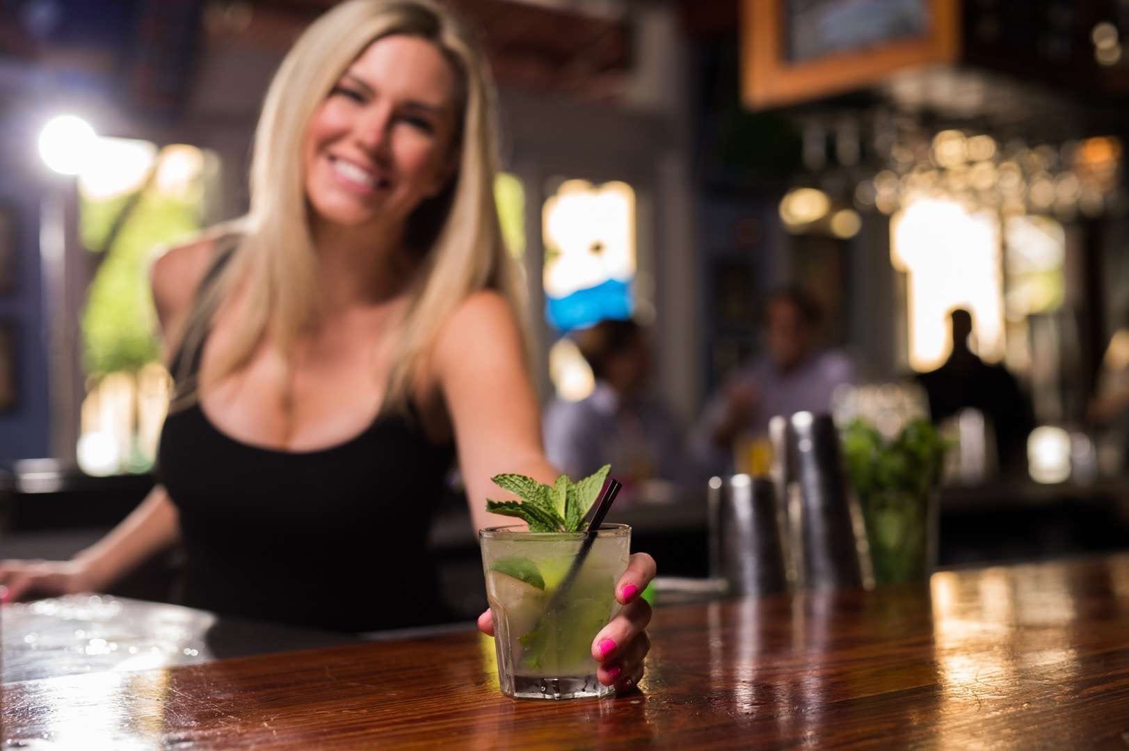 IU C&I Studios Portfolio The Restaurant People Woman with short blond hair in a black crop top smiling and posing with an alcoholic beverage with mint leaves
