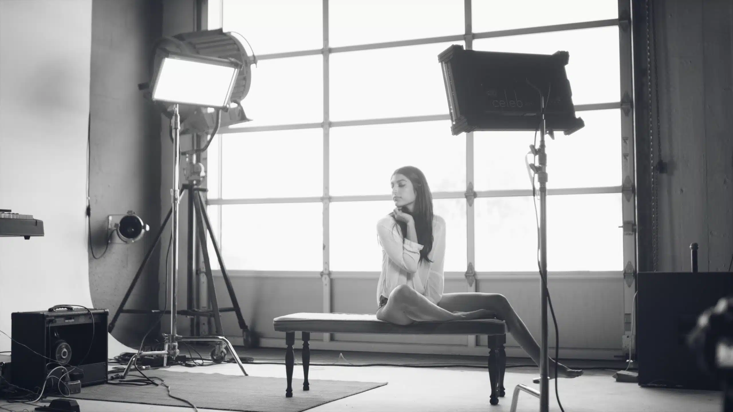 Black and white of Roya posing for the camera sitting on a bench surrounded my visual equipment