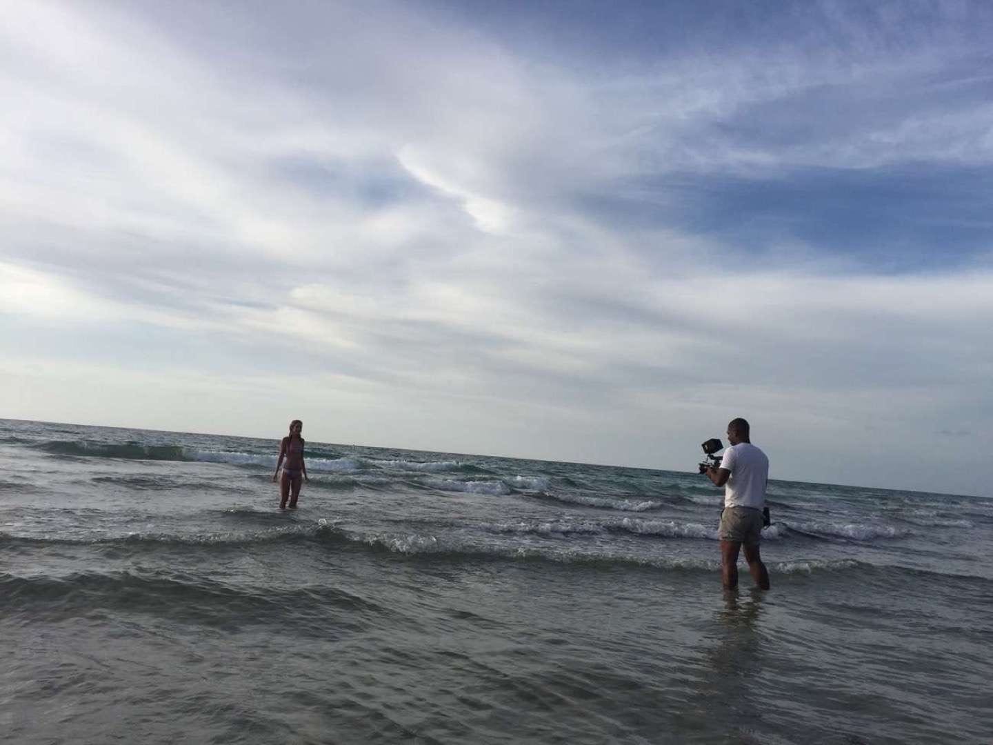 IU C&I Studio CI Studios Portfolio Taylor Adair Swim BTS Young woman in a bikini posing for the camera man standing in the water on a beach