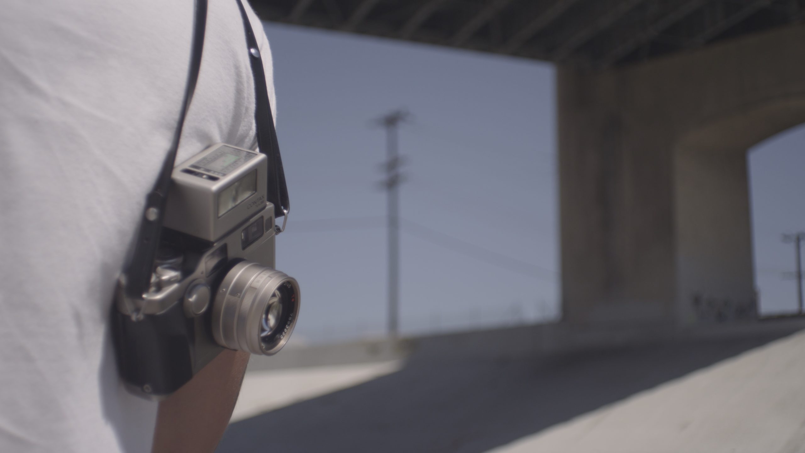 Uncreative Stories Joe Perri Profile Camera being carried over the shoulder by a man by a bridge