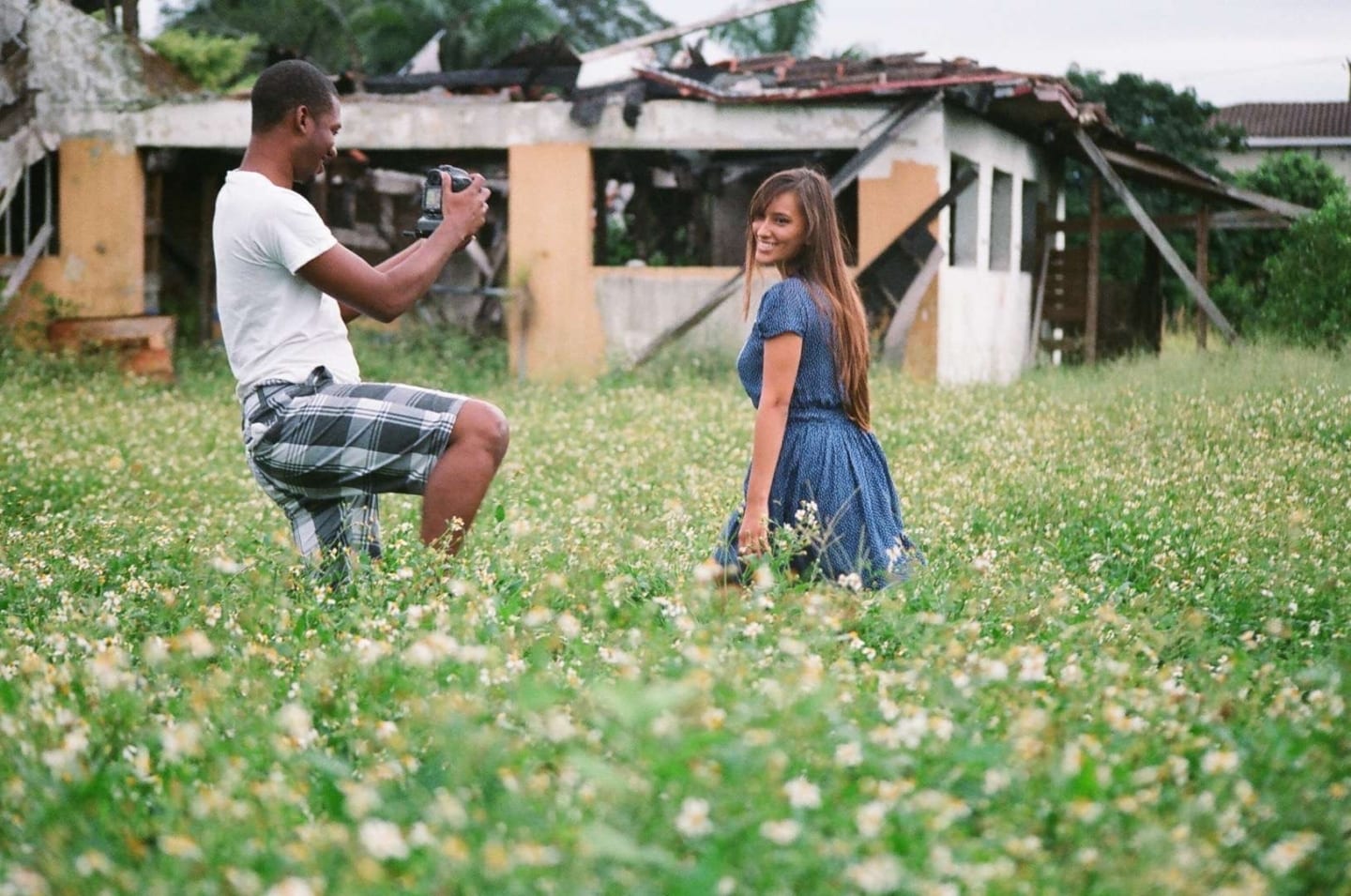 Uncreative Blog Man with video camera filming a woman in a blue dress in a field by ruins of a house