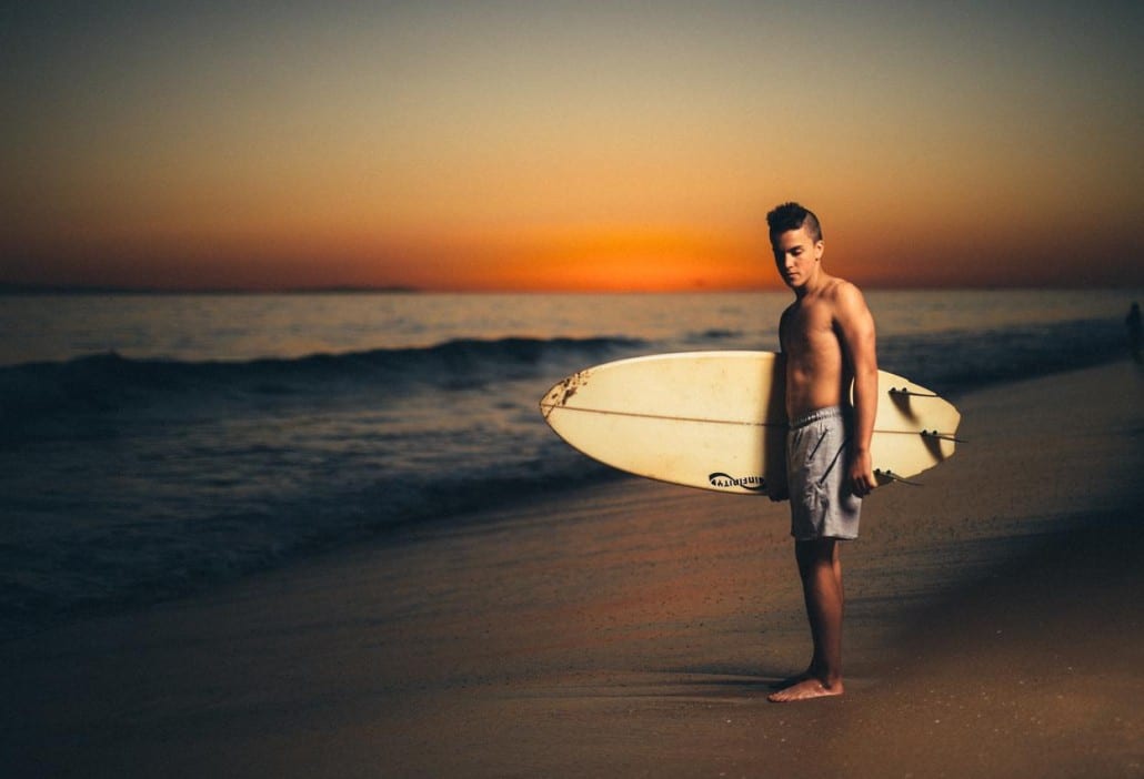 Ivivva Lulu Lemon Young man carrying a surfboard on a beach at dusk