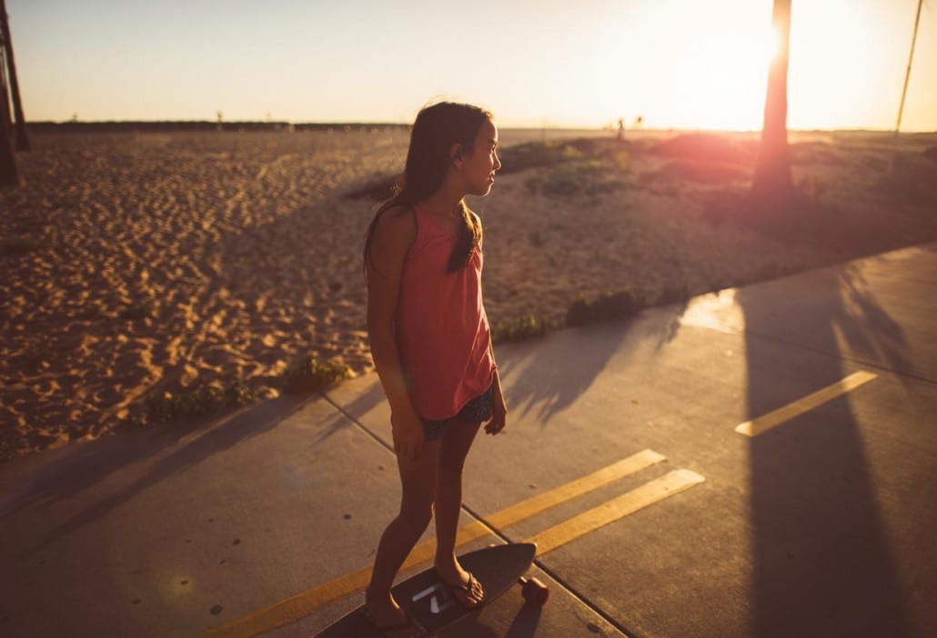 Ivivva Lulu Lemon Girl on a skateboard on a footpath by a beach