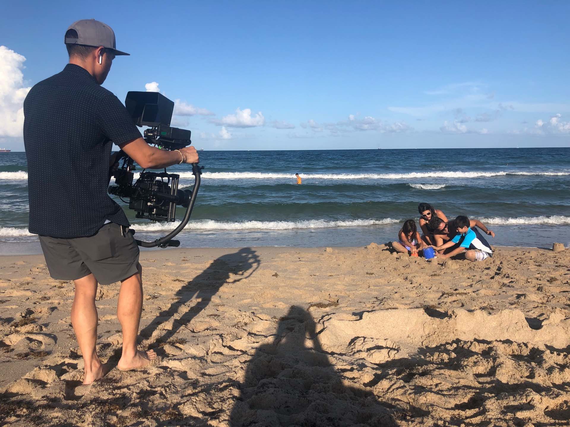 Behind the scenes Video cameraman filming family with two kids playing in the sand at the beach