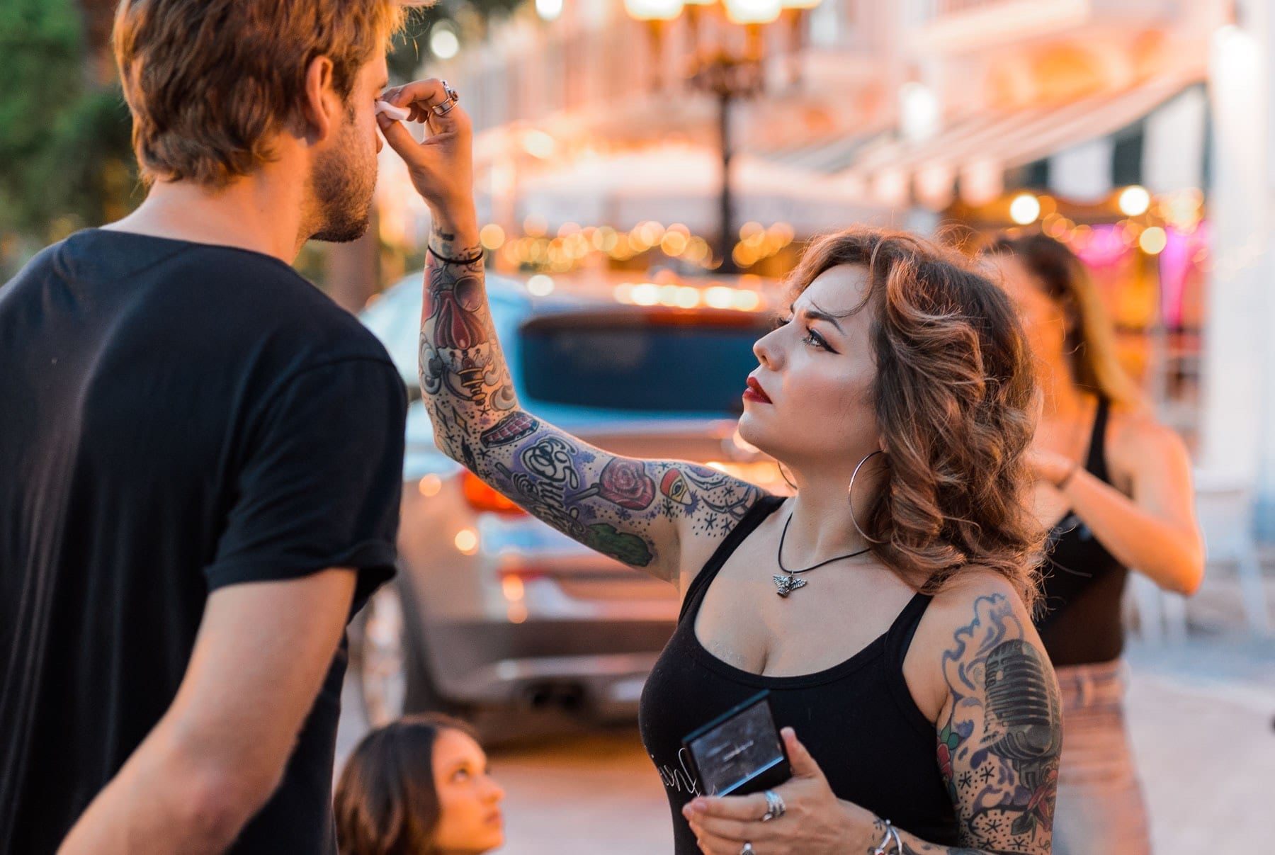 Tattooed makeup artist working on a man with two women nearby
