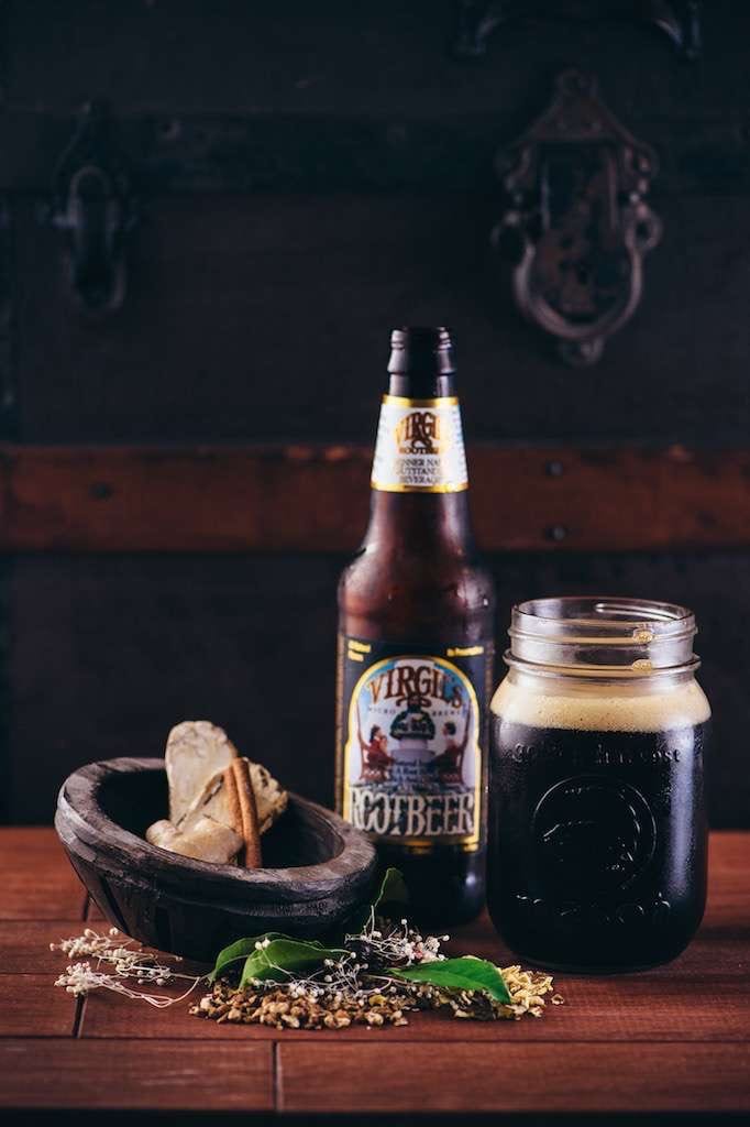 IU CI Studios Portfolio Reeds Closeup of bottle of Virgil's Root Beer as well as a mason jar like cup surrounded by herbs on a wooden table in front of a trunk
