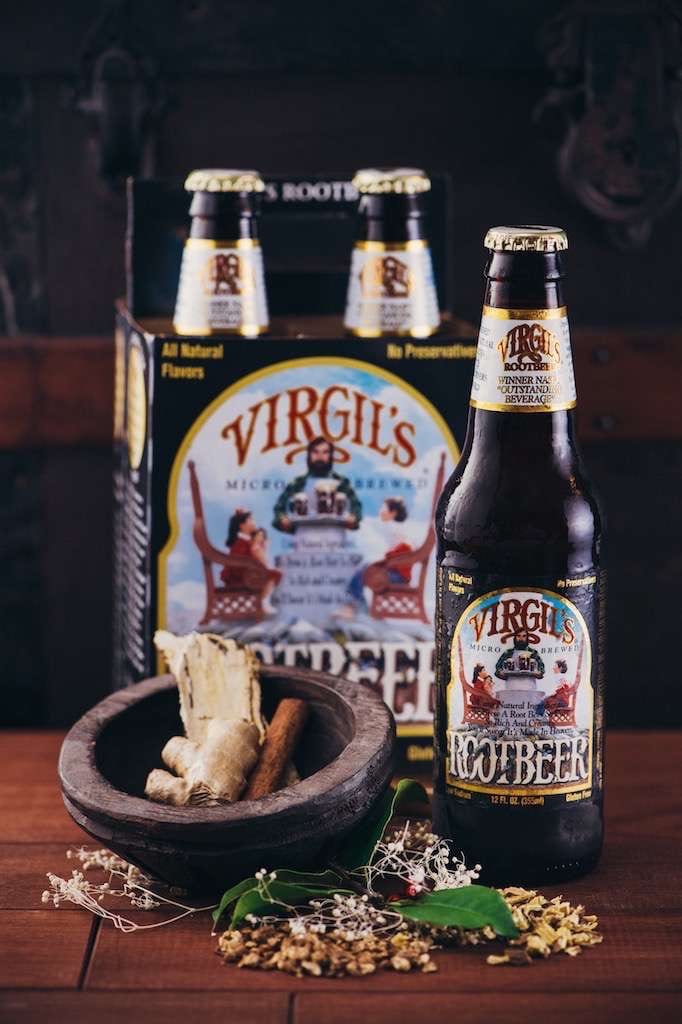 Reeds Bottle of Virgil's Root Beer as well as case surrounded by herbs on a wooden table