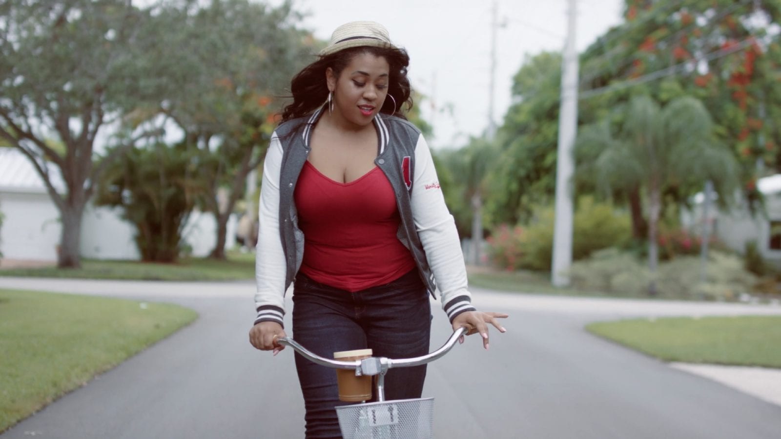 Woman riding a bicycle wearing a white hat, red shirt, light athletic jacket and blue jeans.