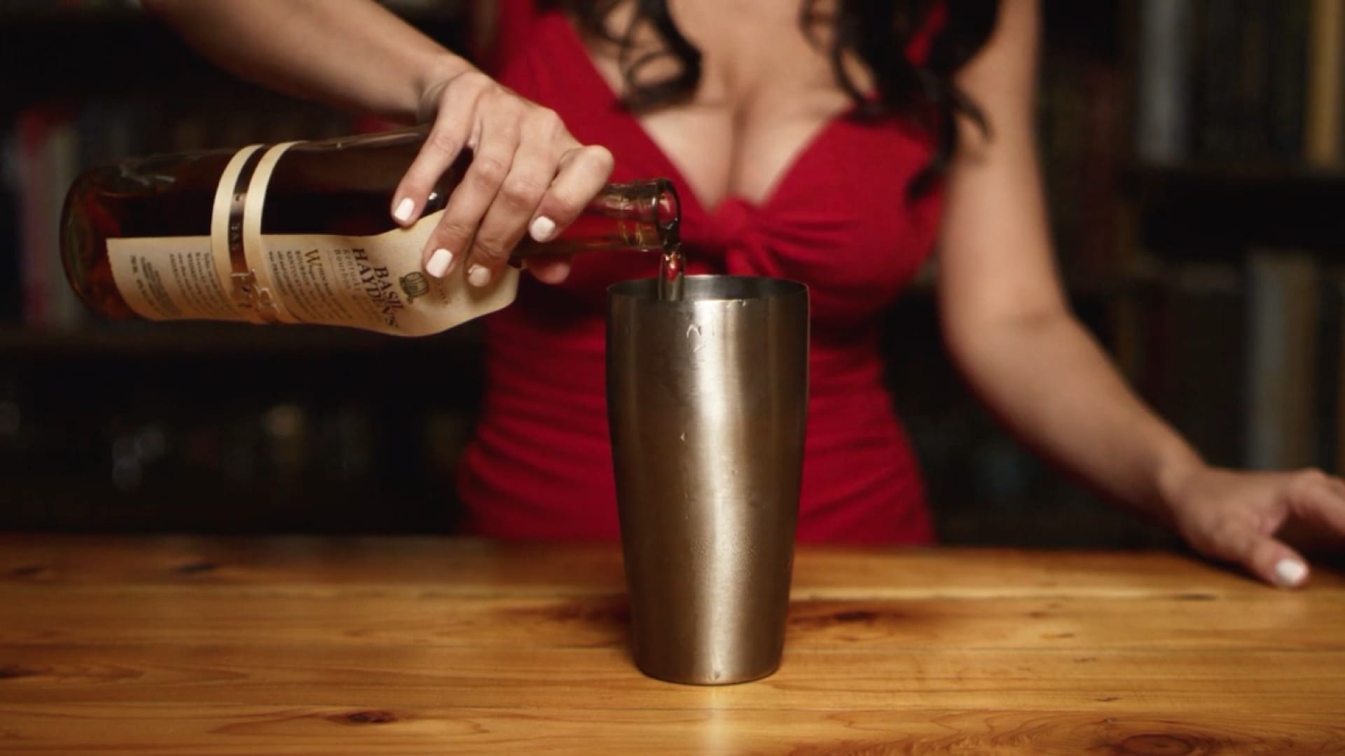 Closeup of a woman in a red dress pouring the drink in a cocktail shaker on a wooden tabel