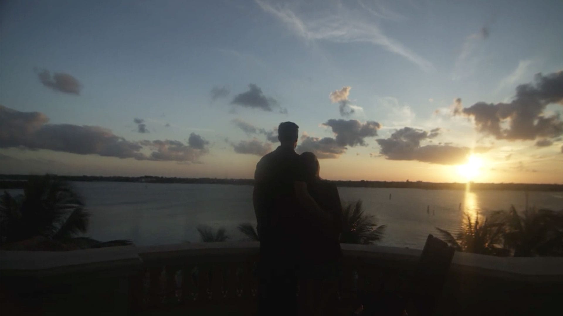 Couple with back to camera looking off into the sunset at a lake at dusk