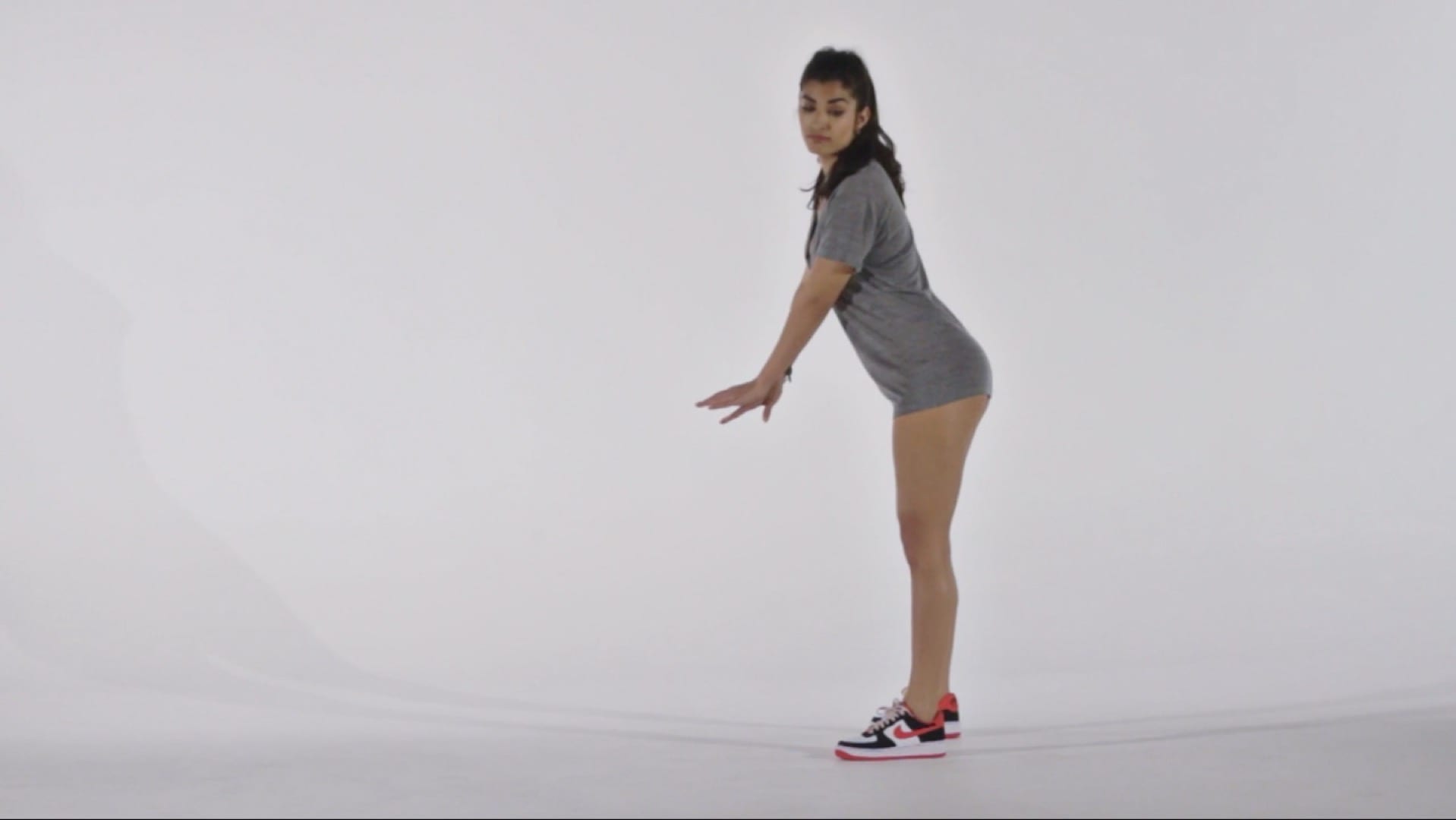 The Archives Sideways profile of model with long black hair wearing a long gray shirt and tennis shoes posing for camera