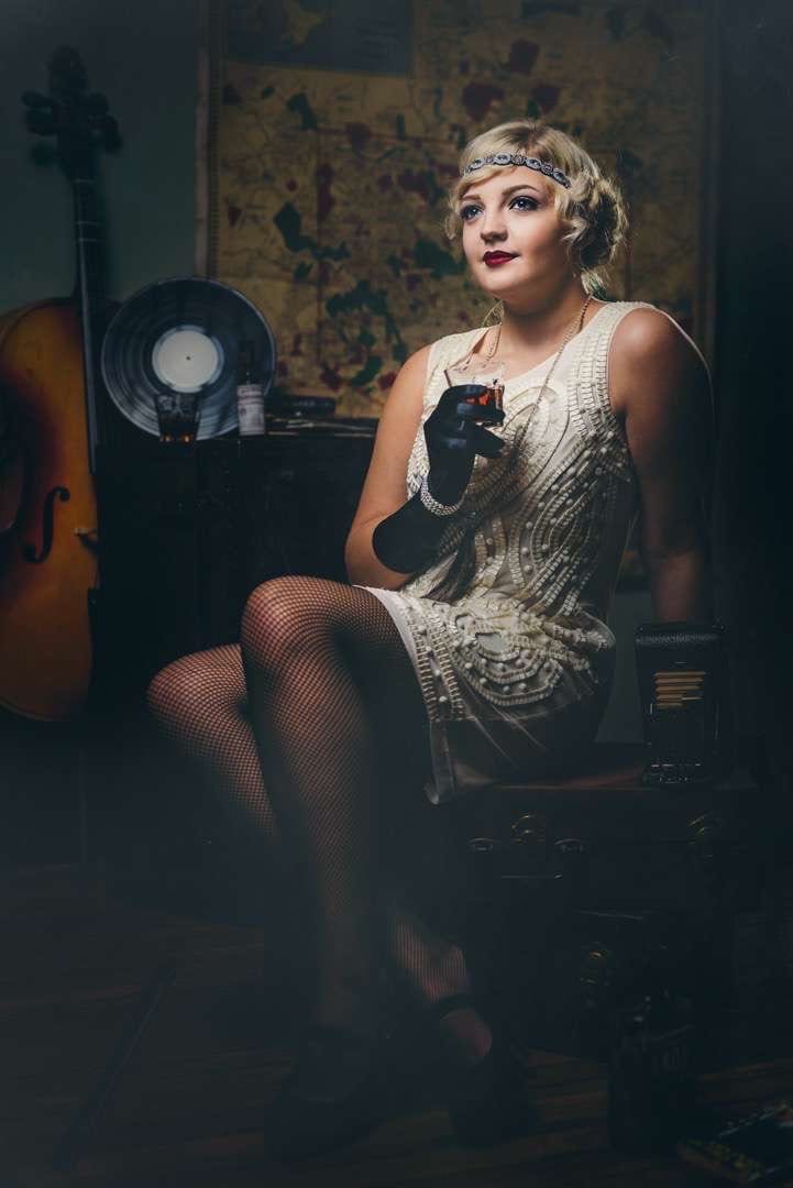 Roarin 20s Portraits Woman in white posing for camera holding a glass of alcohol.