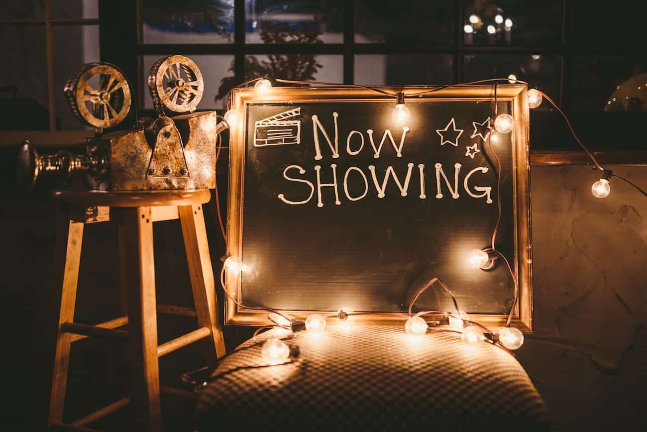 Now Showing sign Mockup of event planning with purpose with makeshift video projector on a wooden stool with a chalkboard sign saying Now Showing with bulb lights,