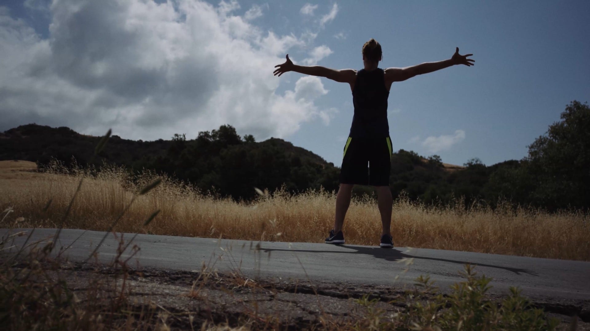 Runner facing away from camera with outstretched arms on a sunny day