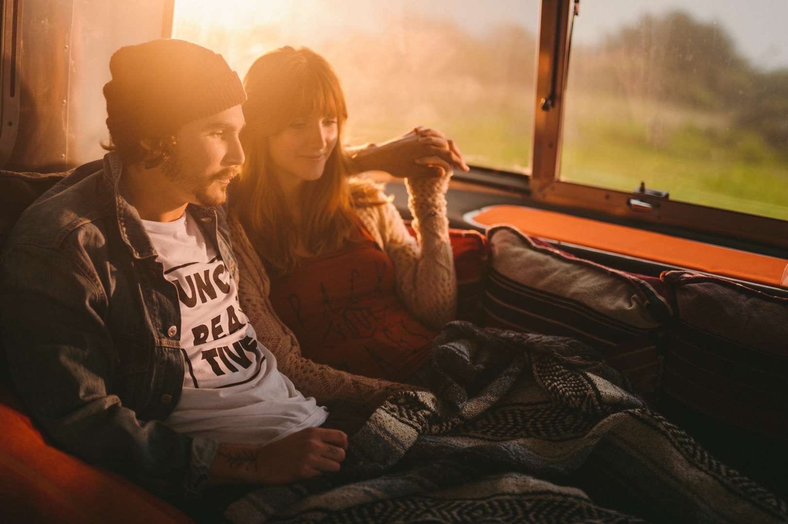 Young man with a tattoo and a young woman relaxing at sunset on a red small couch in a RV.