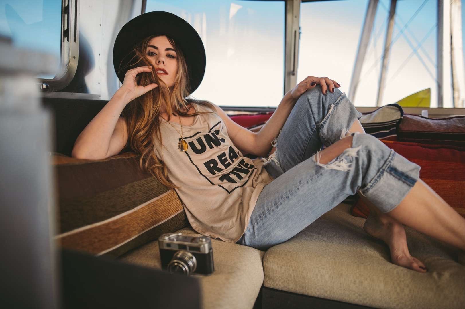 Young woman with long blond hair wearing a black tshirt and jean capris posing for camera from inside a RV with a camera nearby.