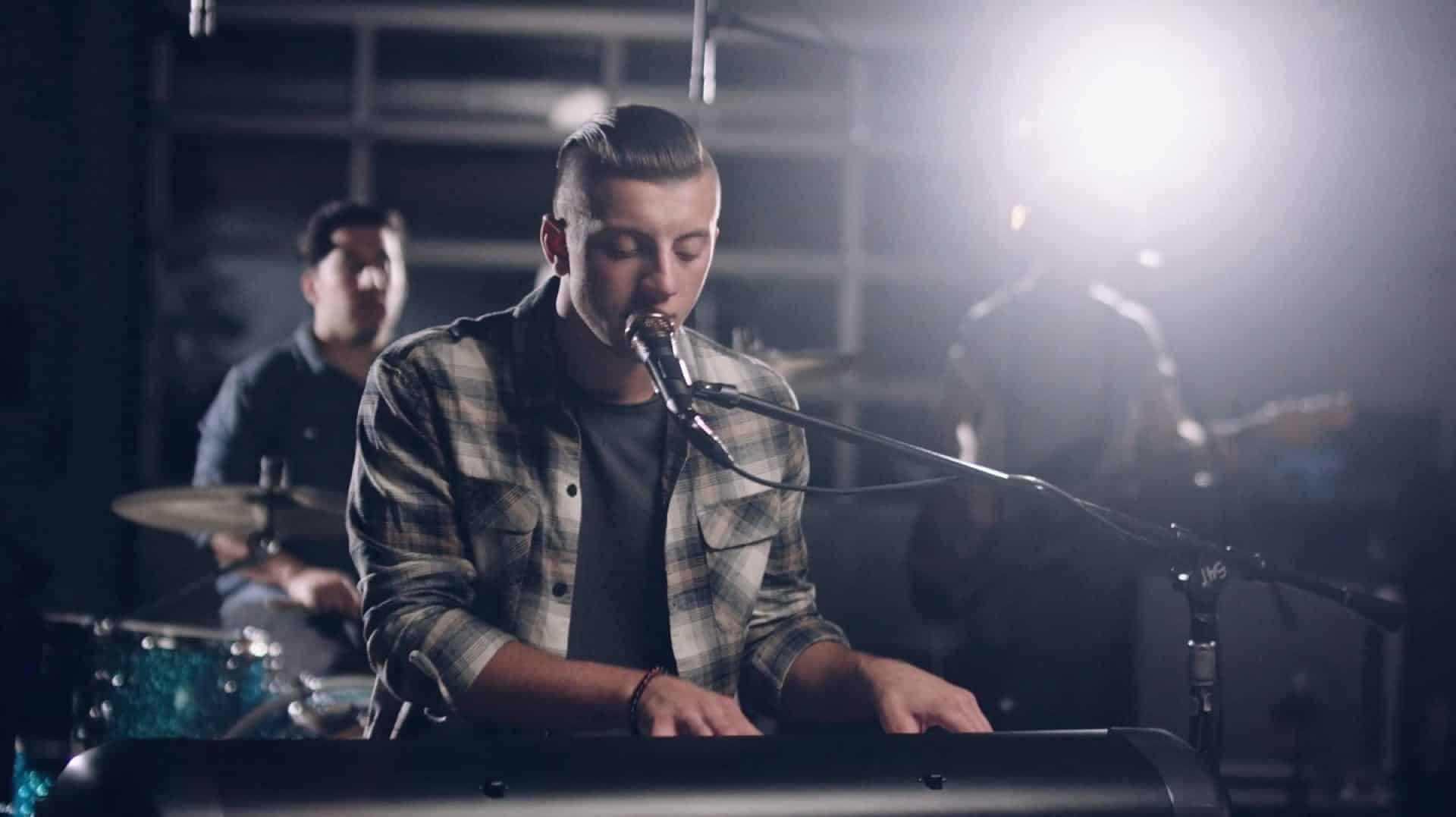 Alexander Di Leo singing at a keyboard in a band with a drummer and guitarist in the background