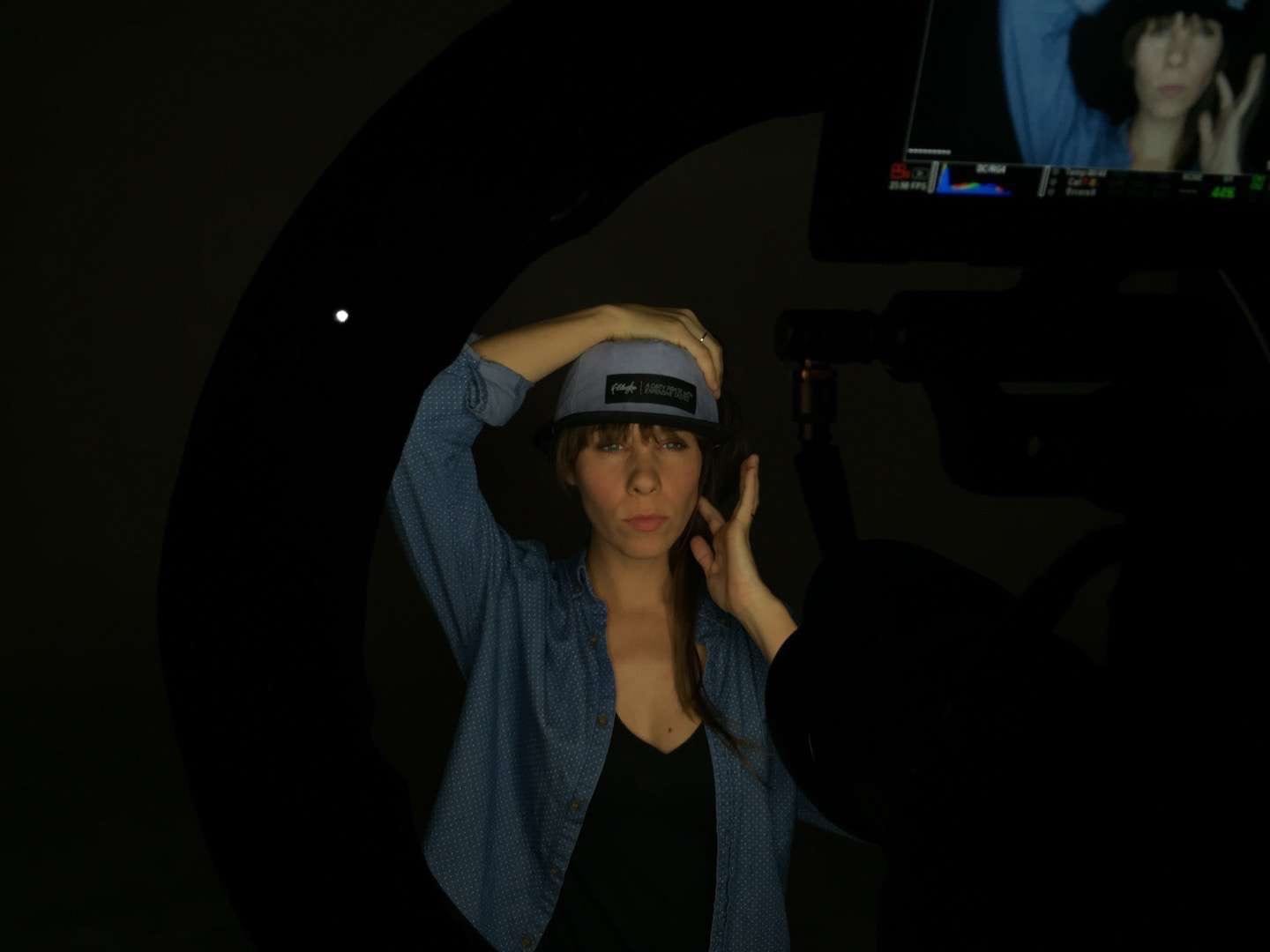 Filibuster Apparel Woman with long brown hair in a blue shirt wearing a gray hat with black rim with video display in foreground