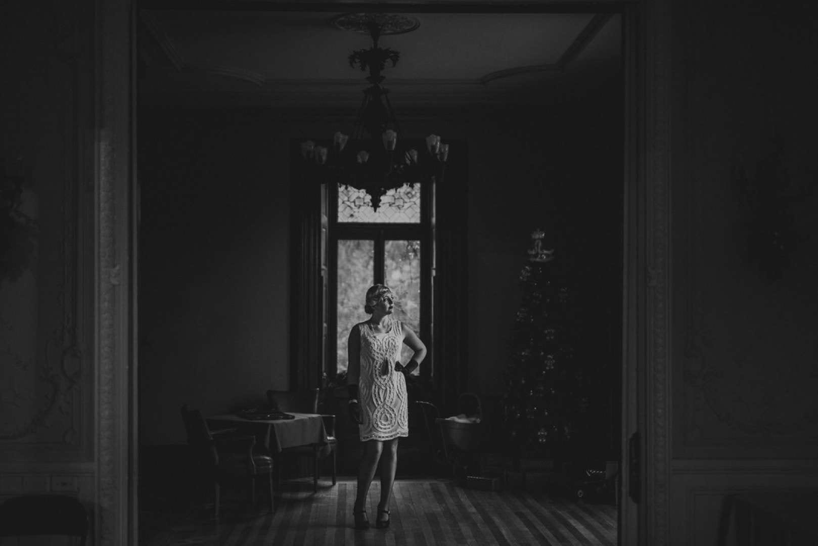 Roarin 20s Portraits Black and white view of a woman standing in an old setup of a room with furniture and a Christmas tree