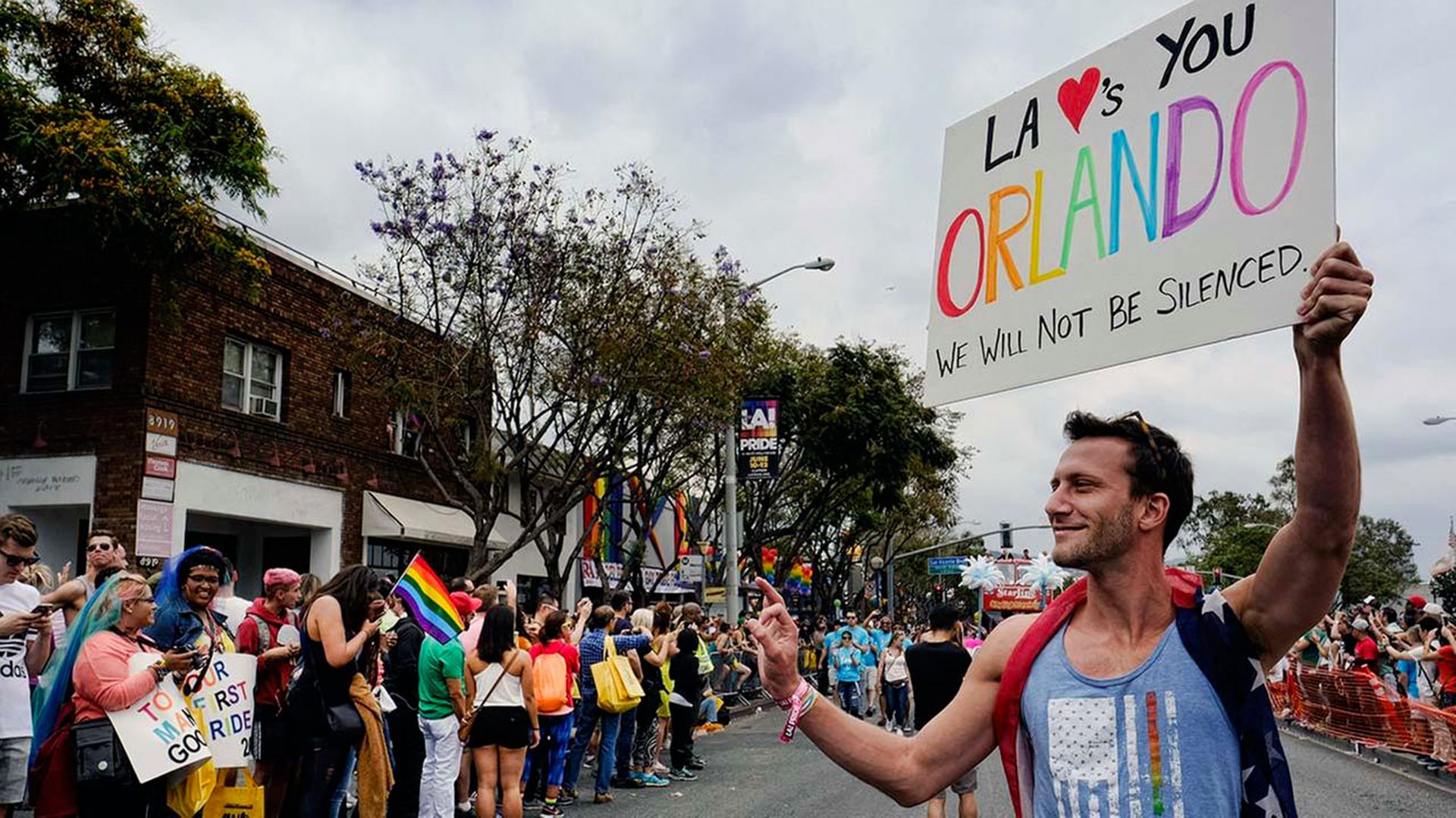 Gay parade in Orlando, Florida with a crowd of people. A man with a flag draped around his neck is carrying a colorful sign.