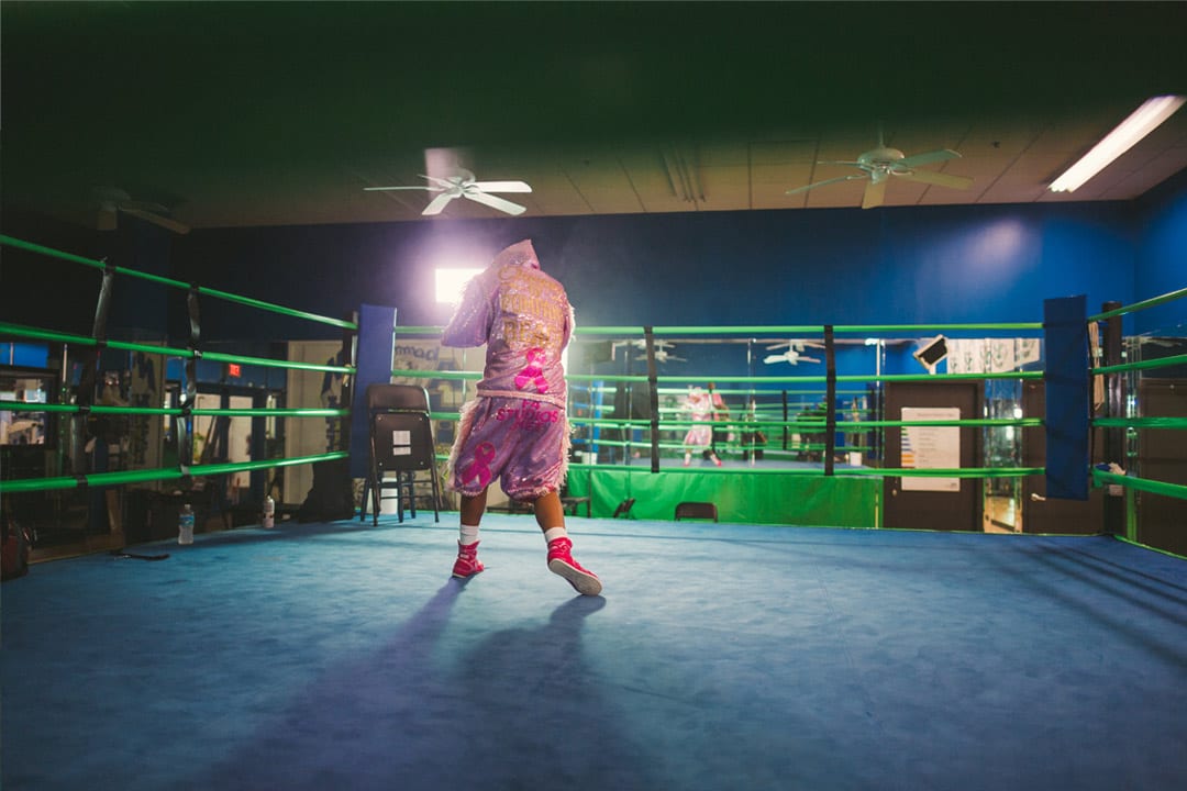Woman in pink outfit facing away from the camera warming up with boxing moves.
