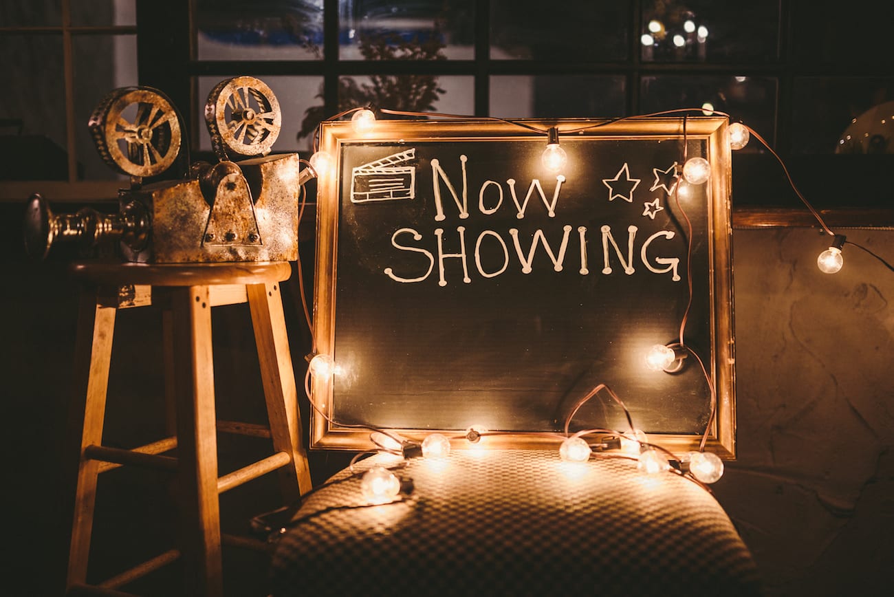 Mockup of event planning with purpose with makeshift video projector on a wooden stool with a chalkboard sign saying Now Showing with bulb lights