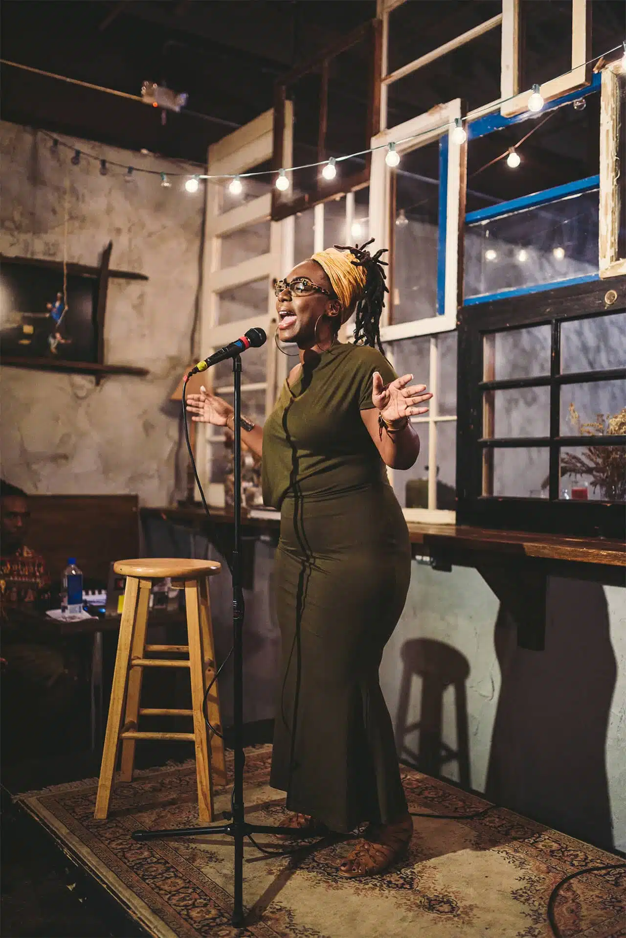 African American woman with olive green dress talking to audience with microphone
