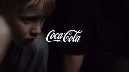 White Coca Cola logo against a background with a young boy