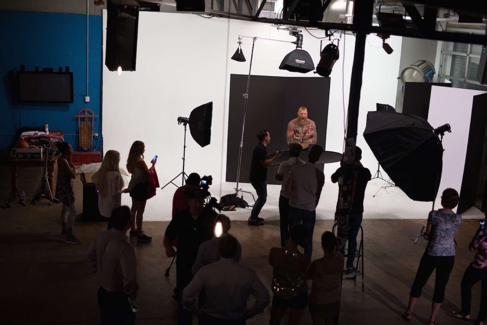 Tattooed man with mohawk posing for camera man and crew holding two Hard Rock Energy drinks