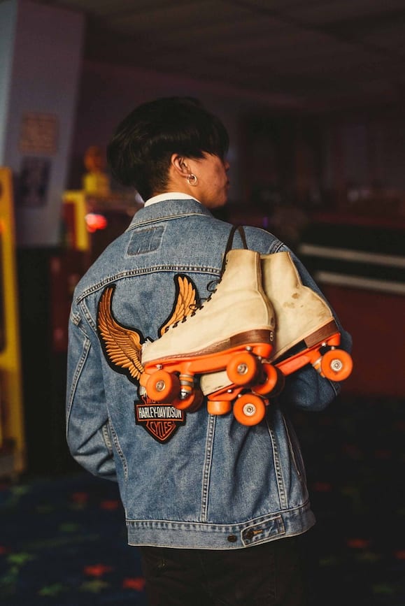 IU CI Studios Social Media Influencer Next Door Marketing View from behind of man wearing jean jacket and carrying a pair of rolling skates with orange wheels on his shoulder