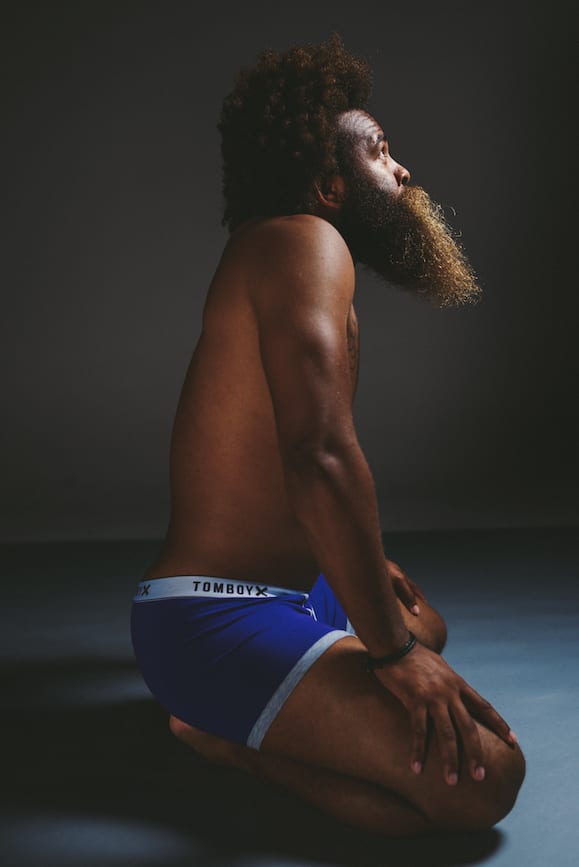 Influencer Marketing Side view of African American man with large beard and curly hair in yoga pose on ground wearing blue briefs