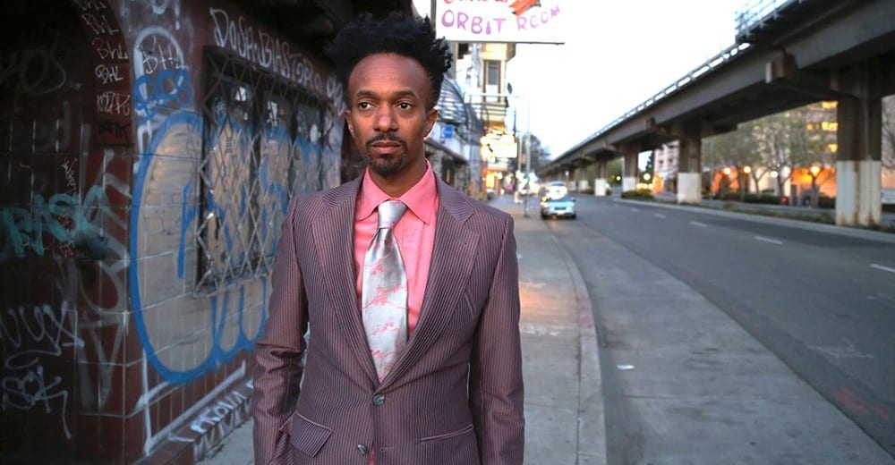 IU C&I Studios Page Artist Profile Fantastic Negrito African American Man posing from street of a city near a bridge