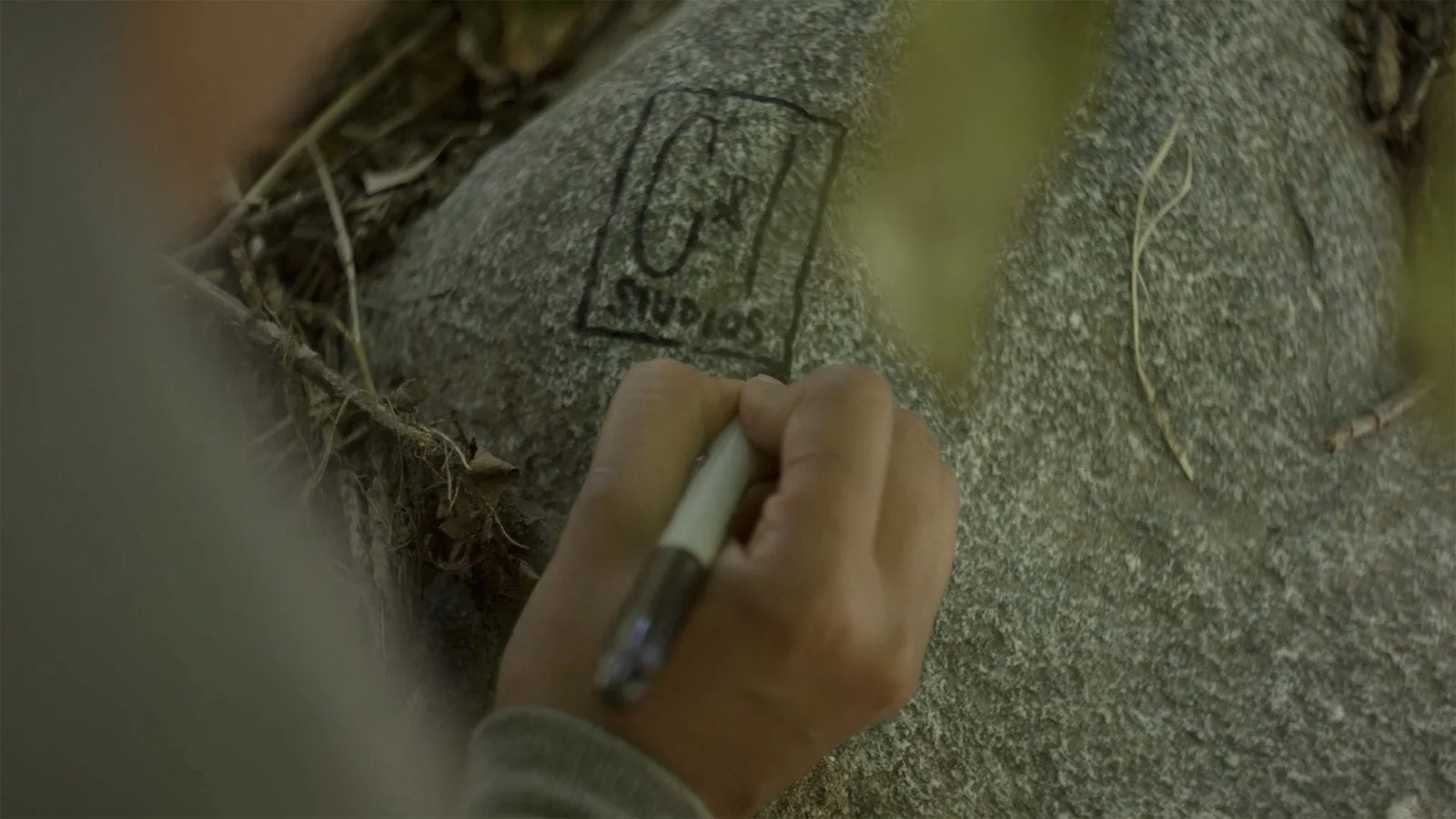 What is C&I Person putting C&I Studios logo on a rock with a black marker pen