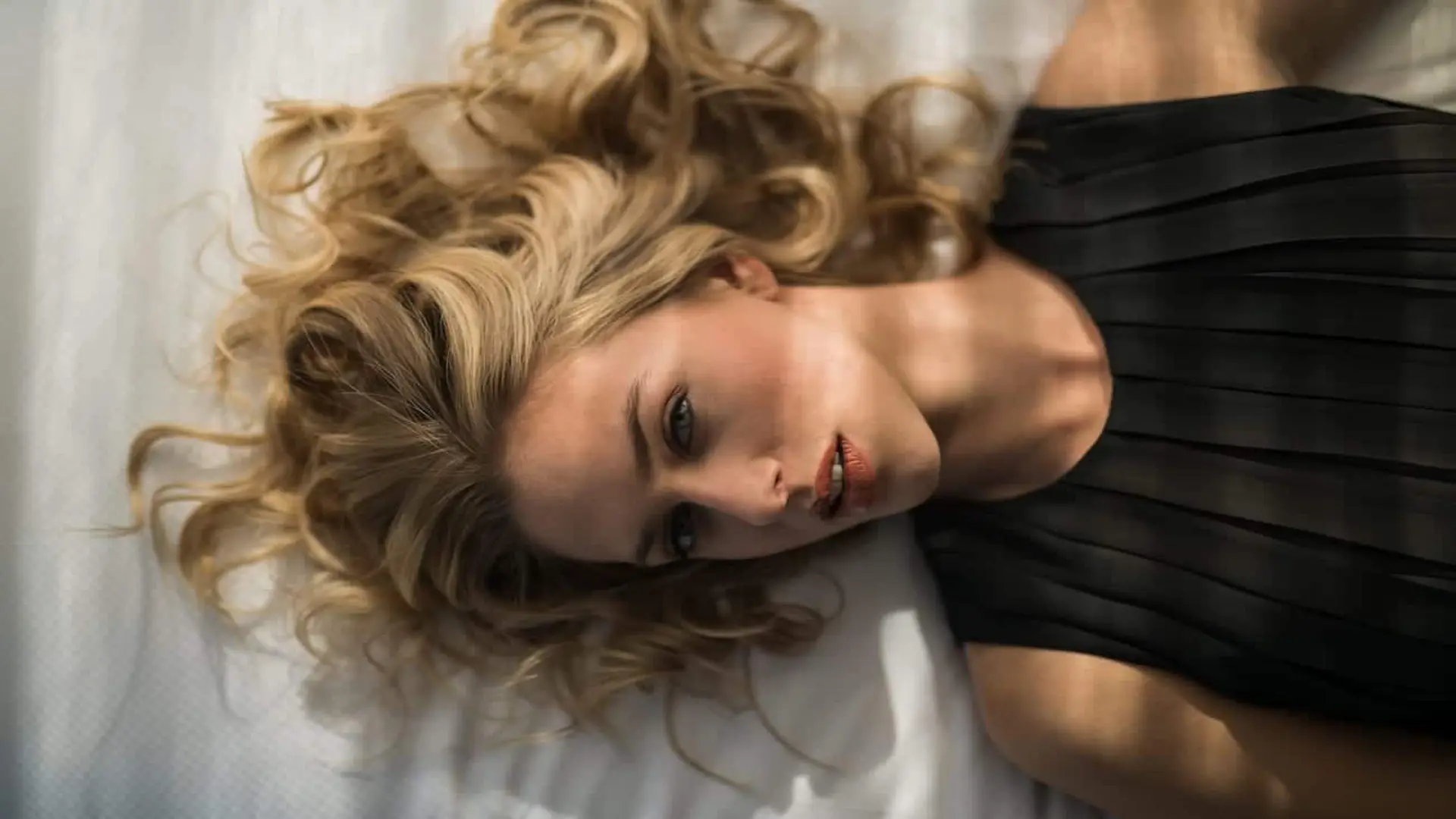 post-facebook-story-ads-social-media-marketing8 View from above of model with curly blond hair wearing a black top laying on bed