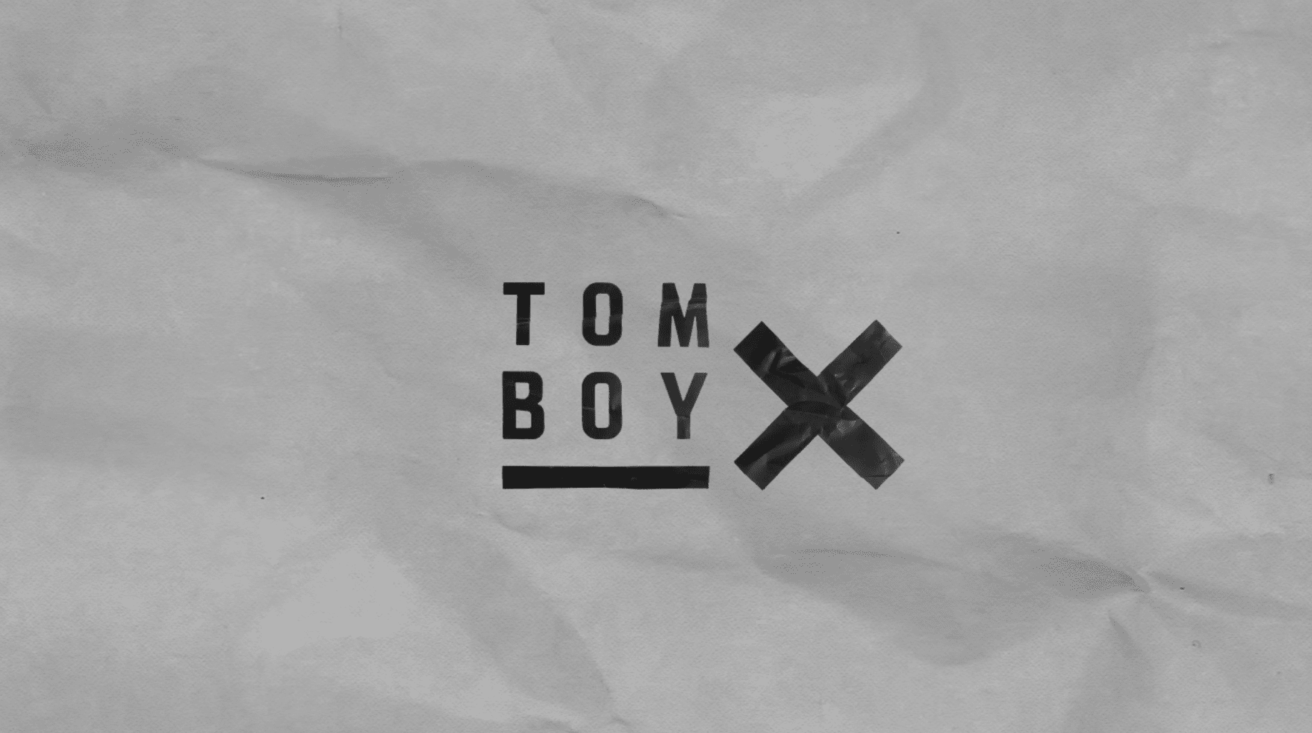 Black Tomboy X logo on crumpled paper background