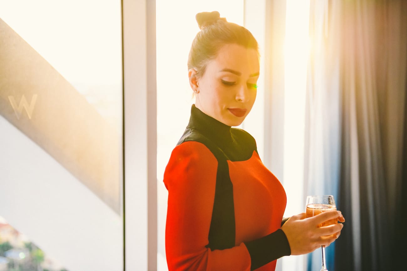 Woman in red and black dress holding a glass of wine looking down posing for camera