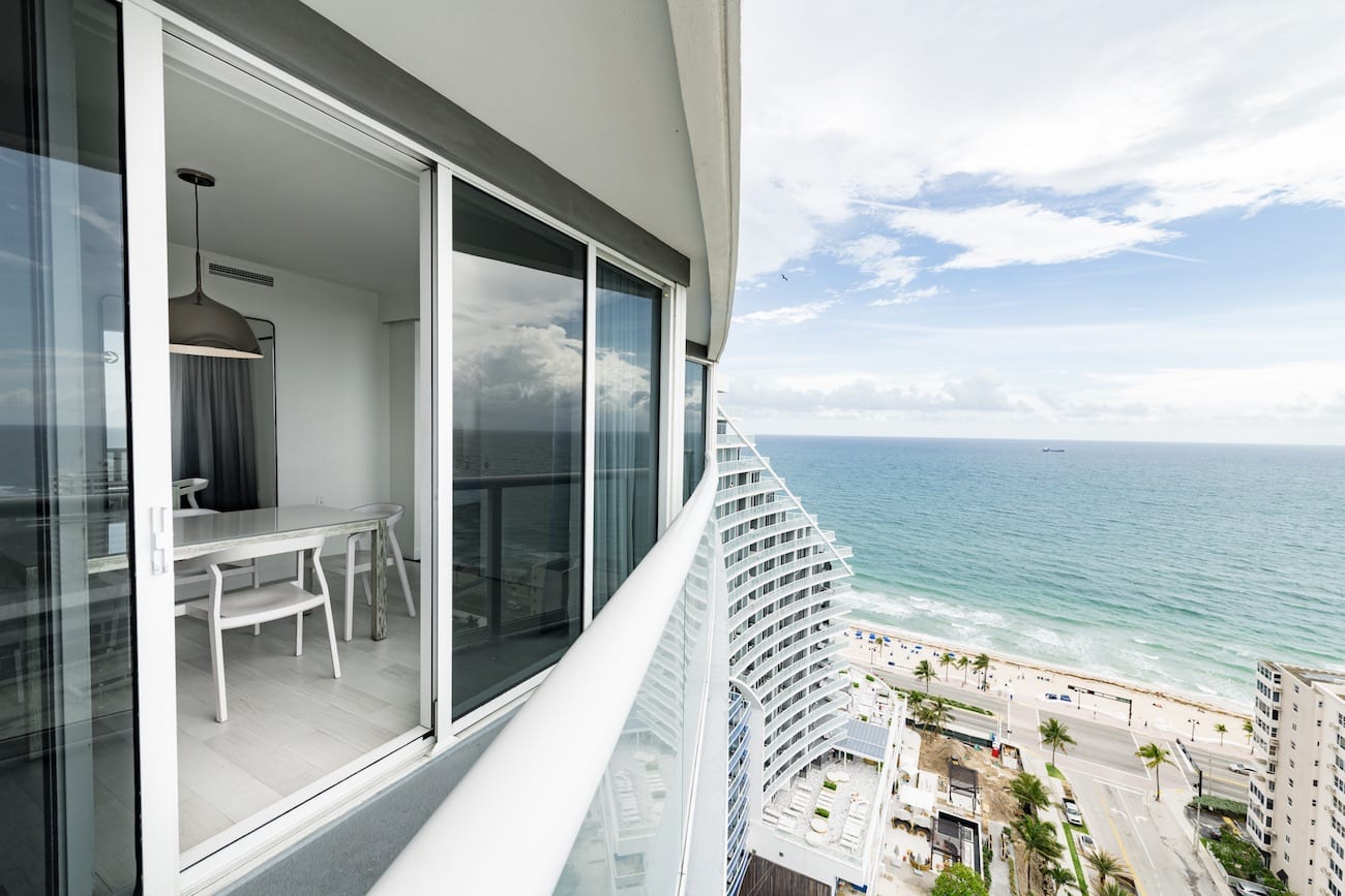 View from balcony looking over beach and city with table and chairs in the background in a room