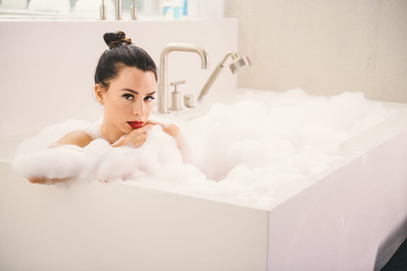 Woman with bright red lipstick in a bubble bath posing for camera leaning on edge of tub