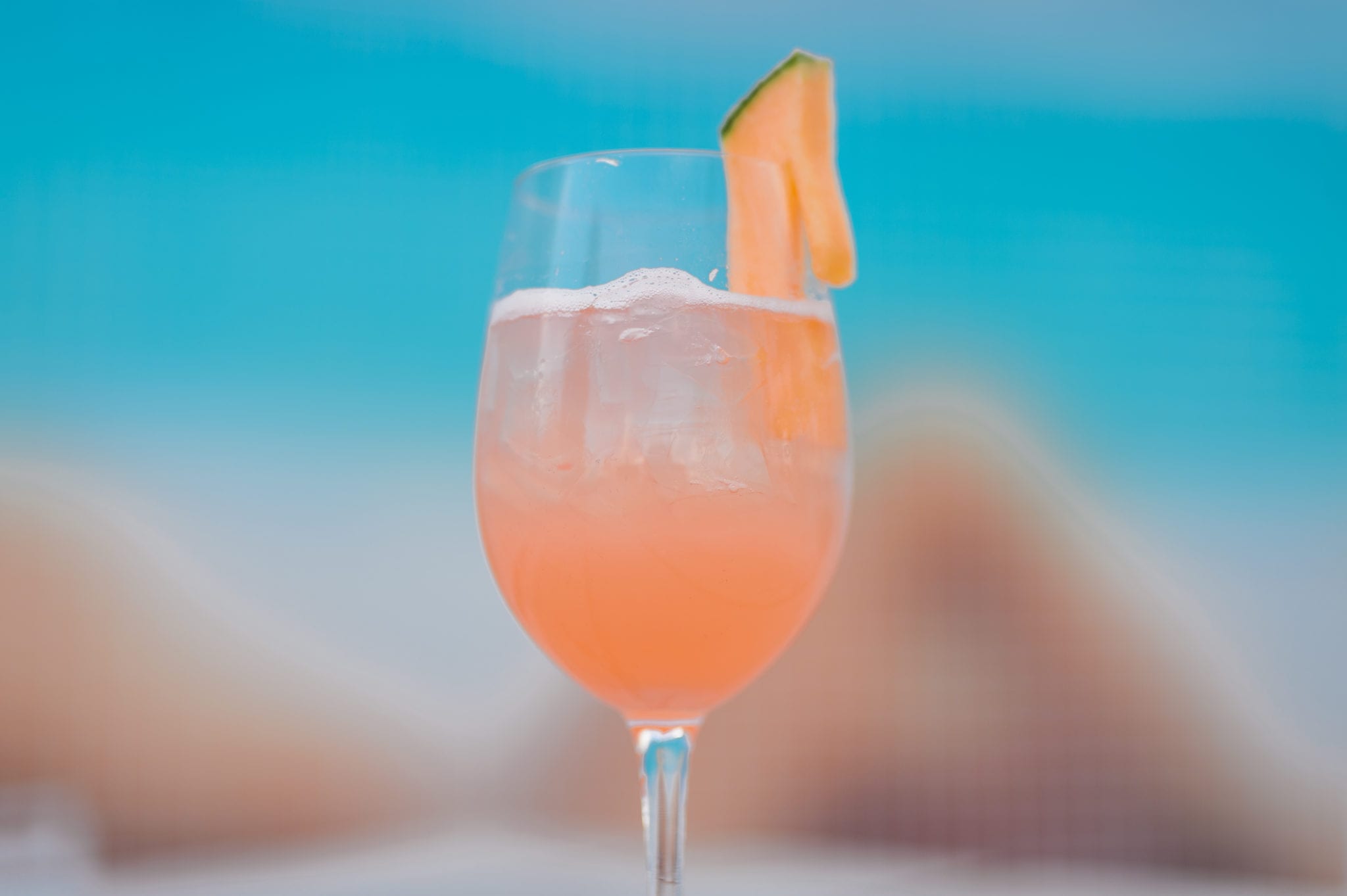 Closeup of a pink drink with a slice of cantaloupe on the rim in a glass