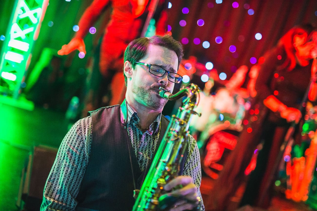 Man with glasses and eyes closed playing a saxophone in a band