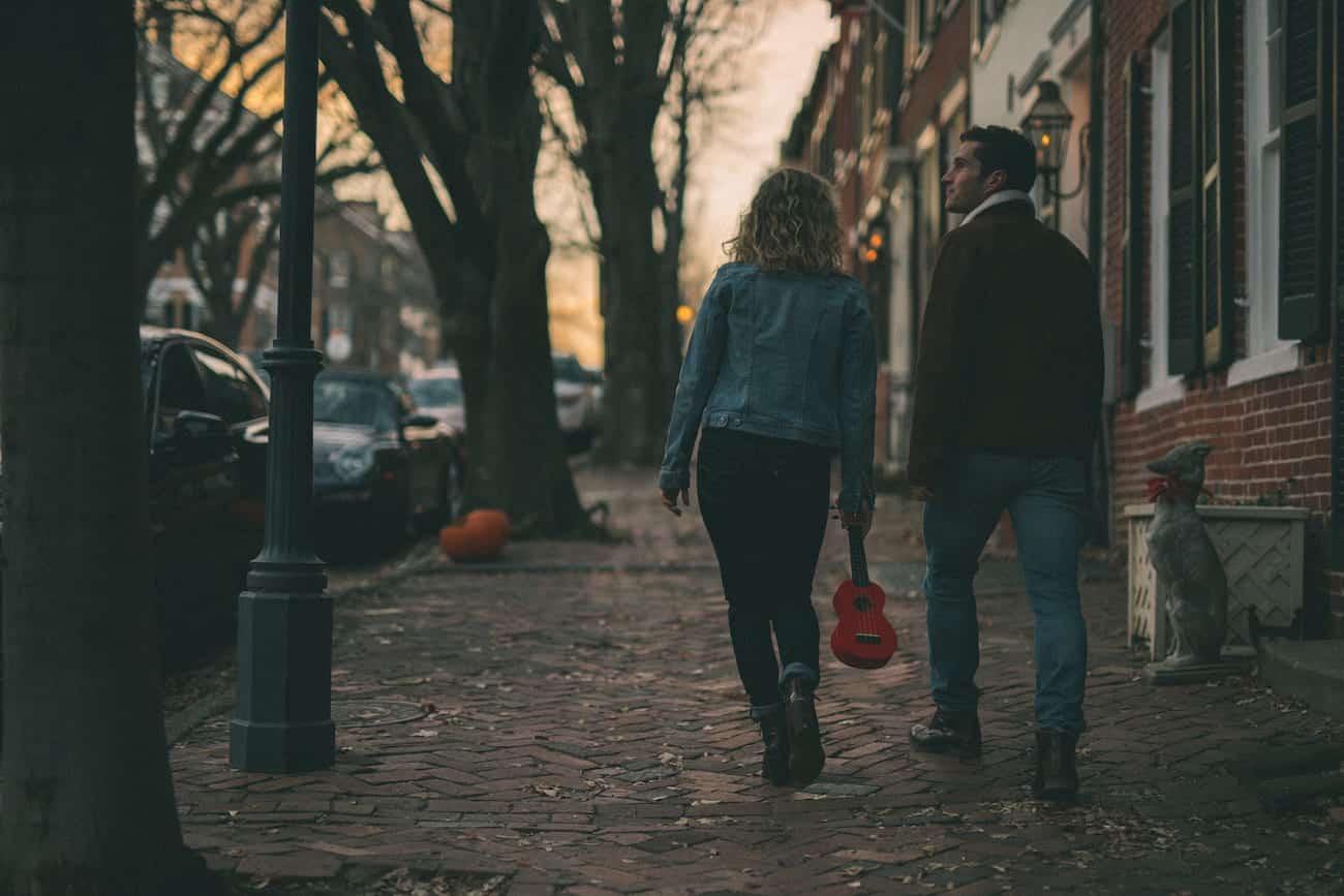 Man and woman walking down a city street with the woman holding a small red guitar