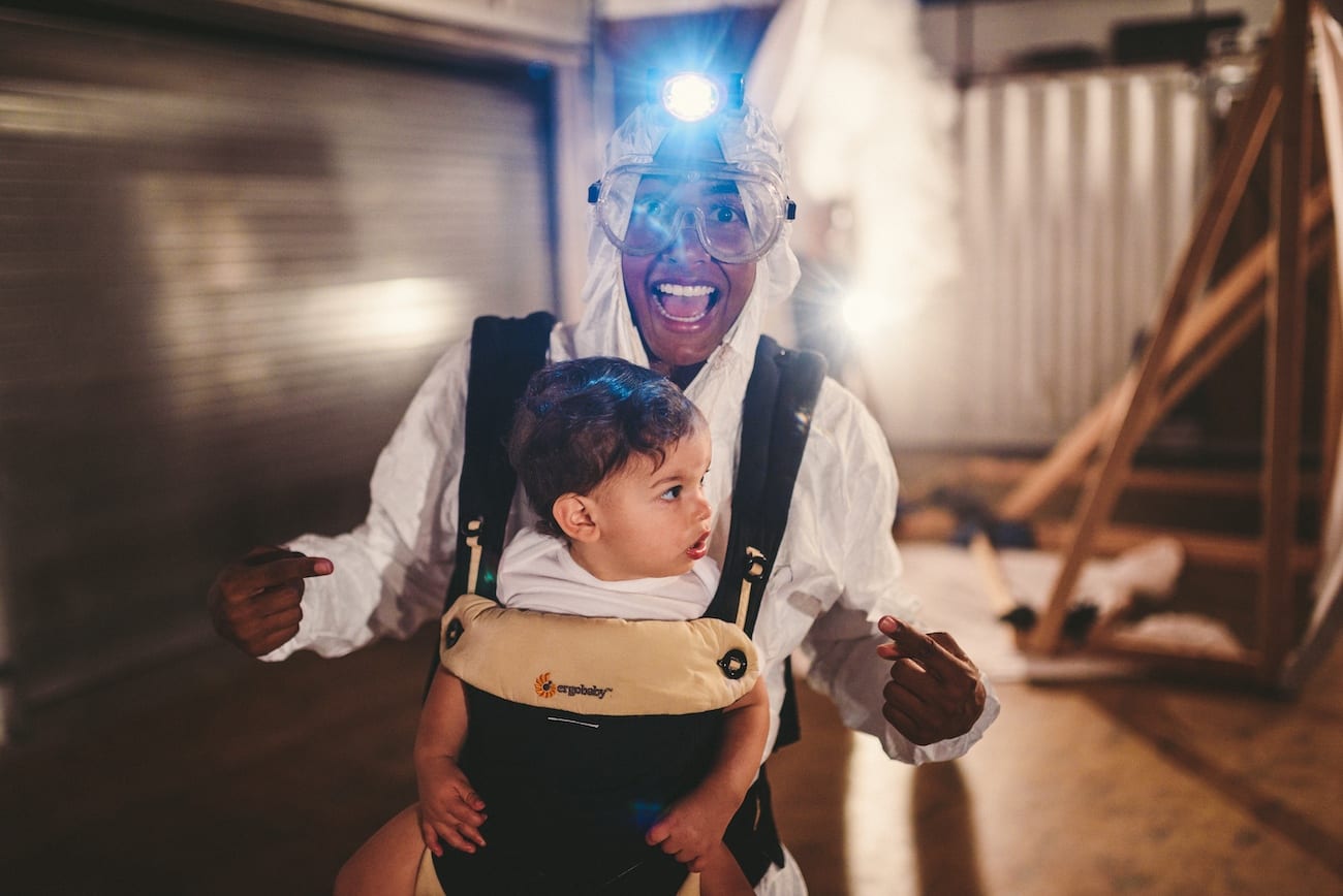 Viral Video Marketing by C&I studios Woman wearing a hazmat suit wearing goggles and carrying a baby on the front smiling and posing for the camera