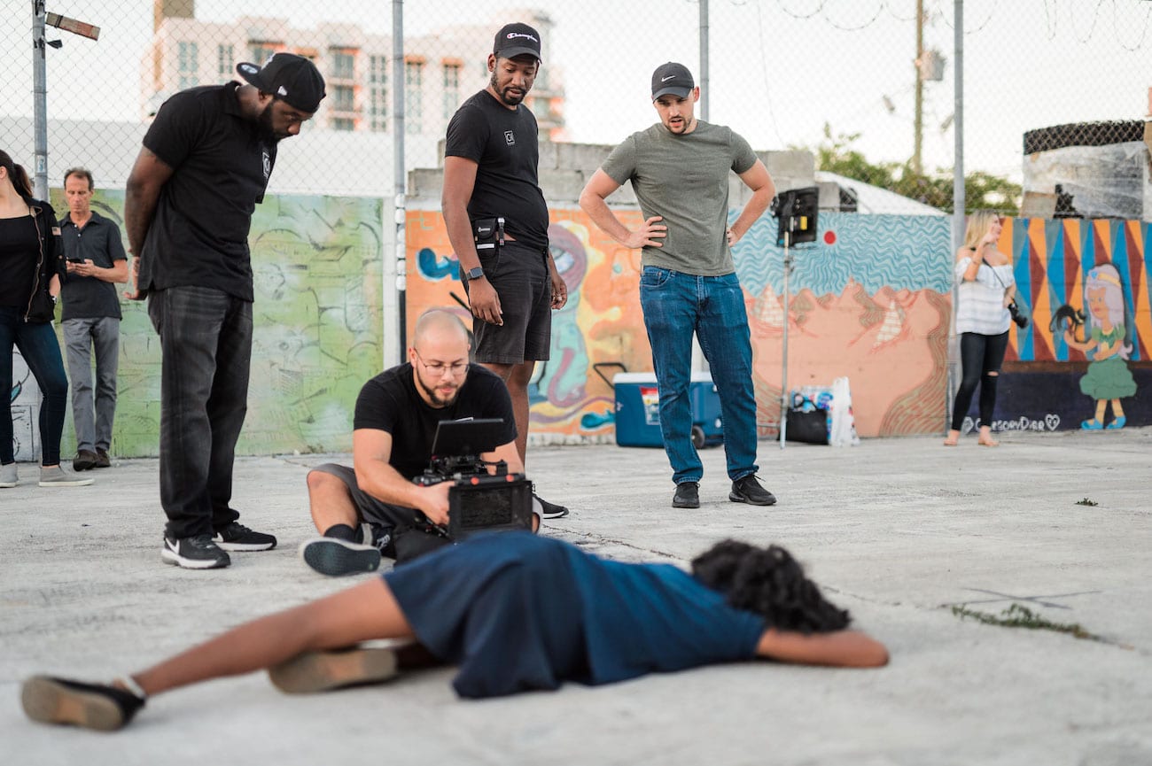 IU C&I Studios Portfolio OneUnited BTS 25 Advertising Agency in Fort Lauderdale View from behind of protester being filmed by video cameraman laying on the ground