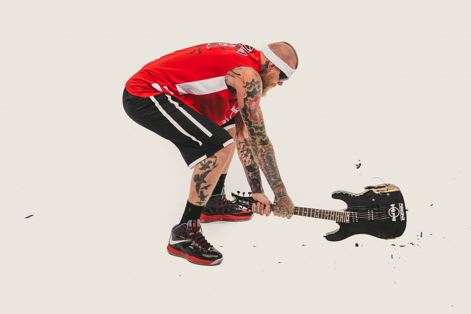 Hard Rock Energy Marketing by C&I Studios Side profile of a bearded tattooed man wearing sunglasses slamming a guitar on the floor wearing red Hard Rock Energy jersey with black shorts