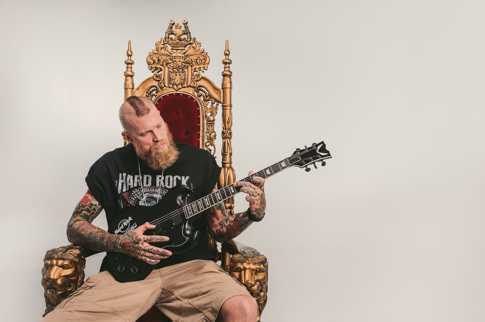 Hard Rock Energy Marketing by C&I Studios Bearded tattooed man playing a guitar on a throne posing for camera wearing a black Hard Rock tshirt