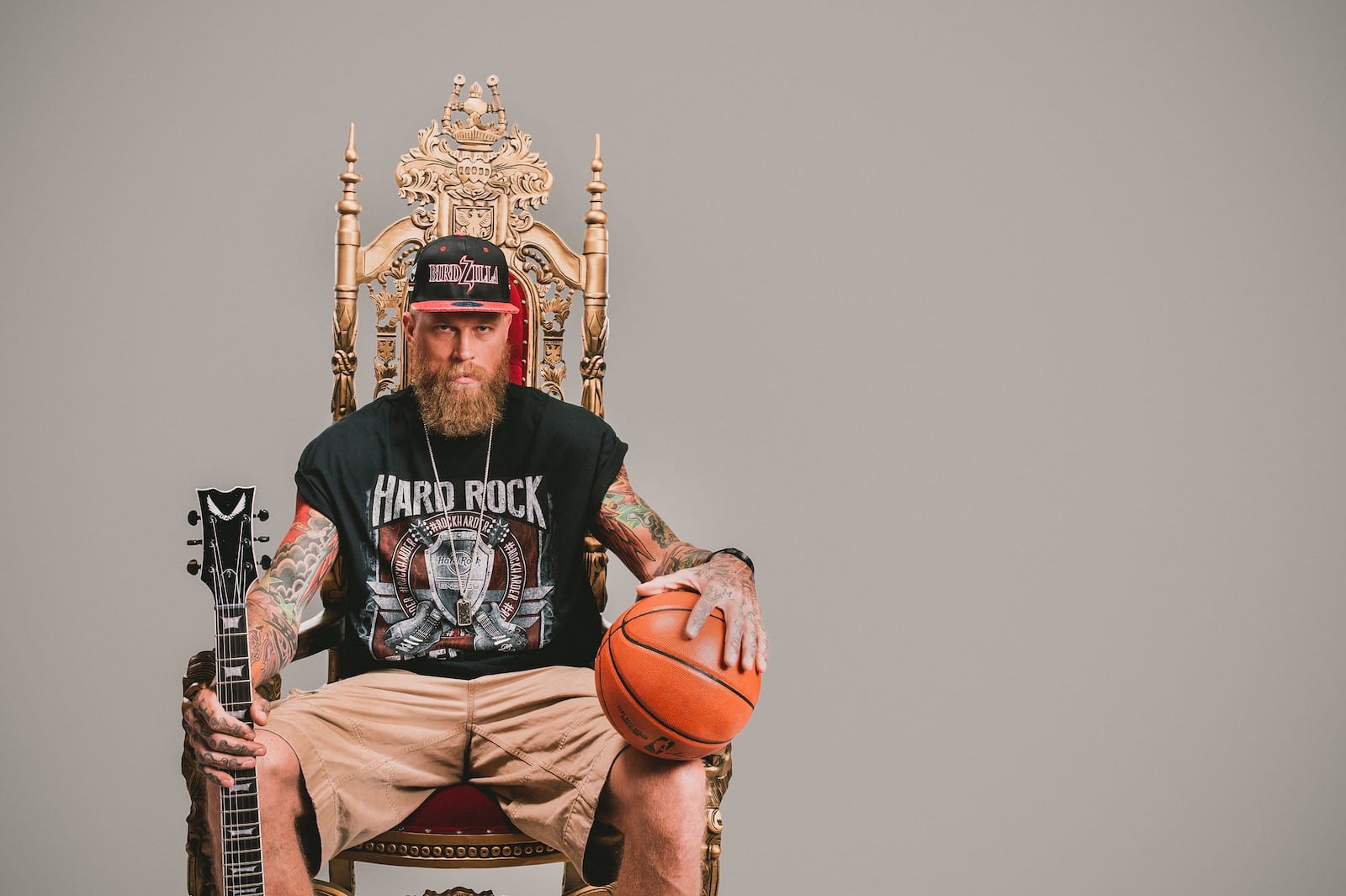 Hard Rock Energy Marketing by C&I Studios Bearded tattooed man holding guitar in one hand and a basketball in the other sitting on a throne posing for camera wearing a black Hard Rock tshirt