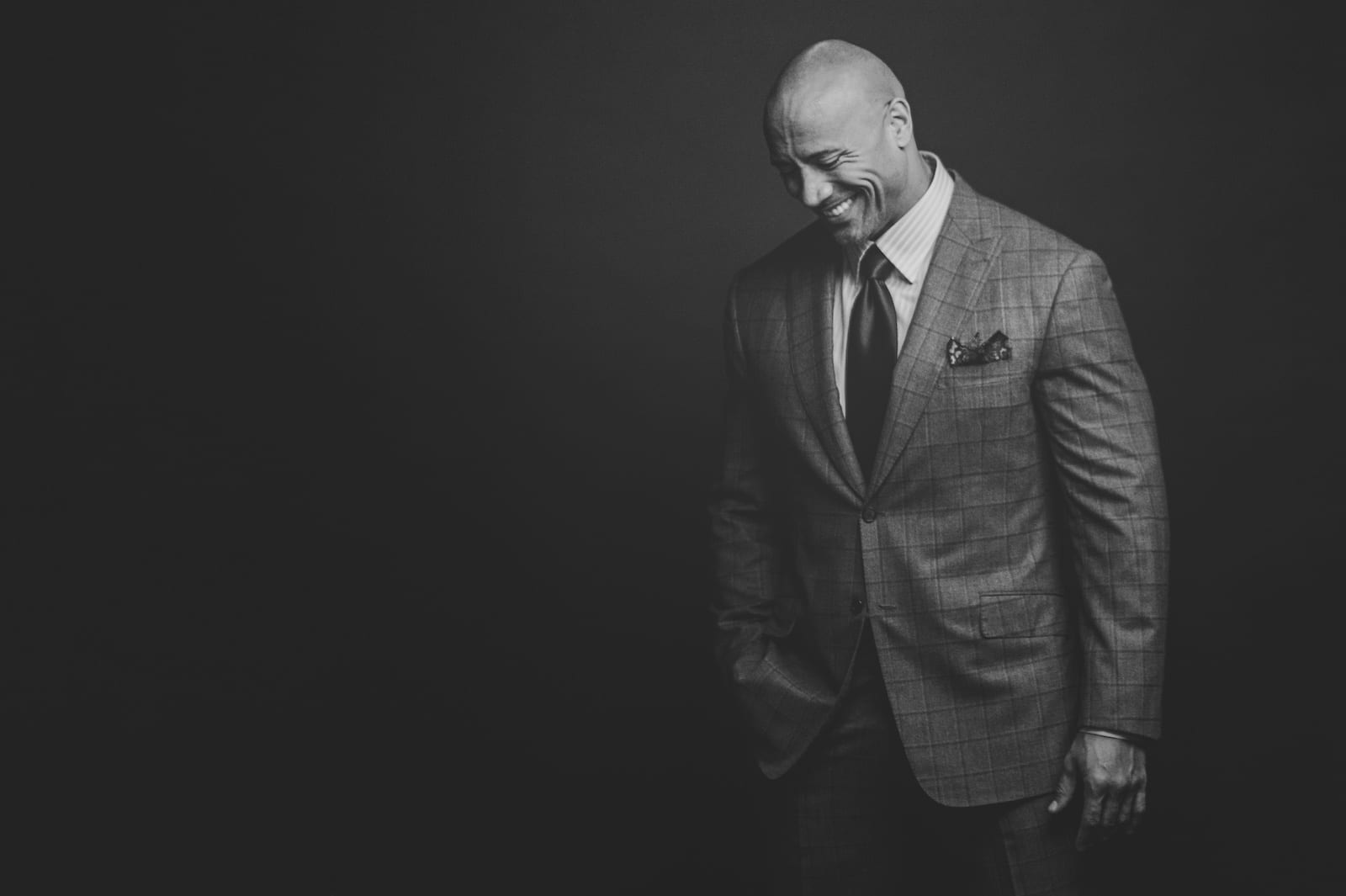 Black and white of Dwayne "The Rock" Johnson with Fortune Magazine posing for camera looking down and smiling